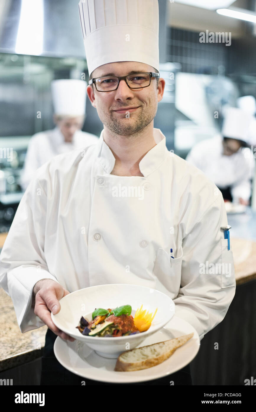 A caucasian male chef presenting a finished plate of fish in a commercial kitchen Stock Photo