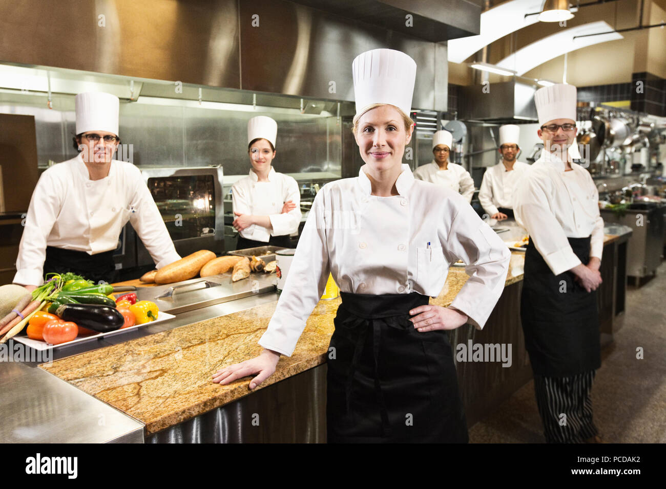 A portrait of a caucasian female chef and her team of chefs in the backgroiund. Stock Photo