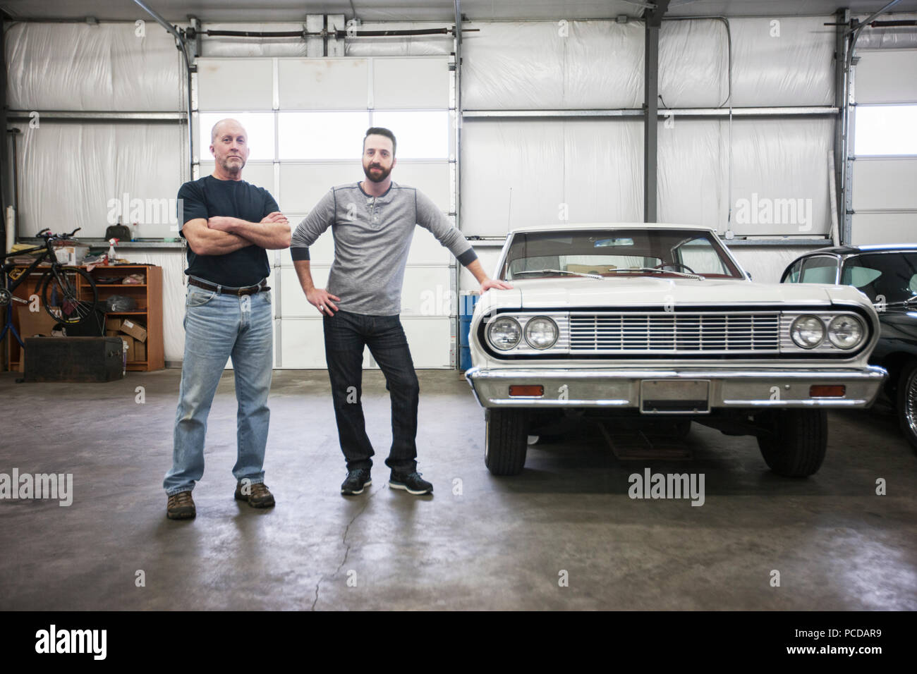 A portrait of a caucasian senior car mechanic and his son in their