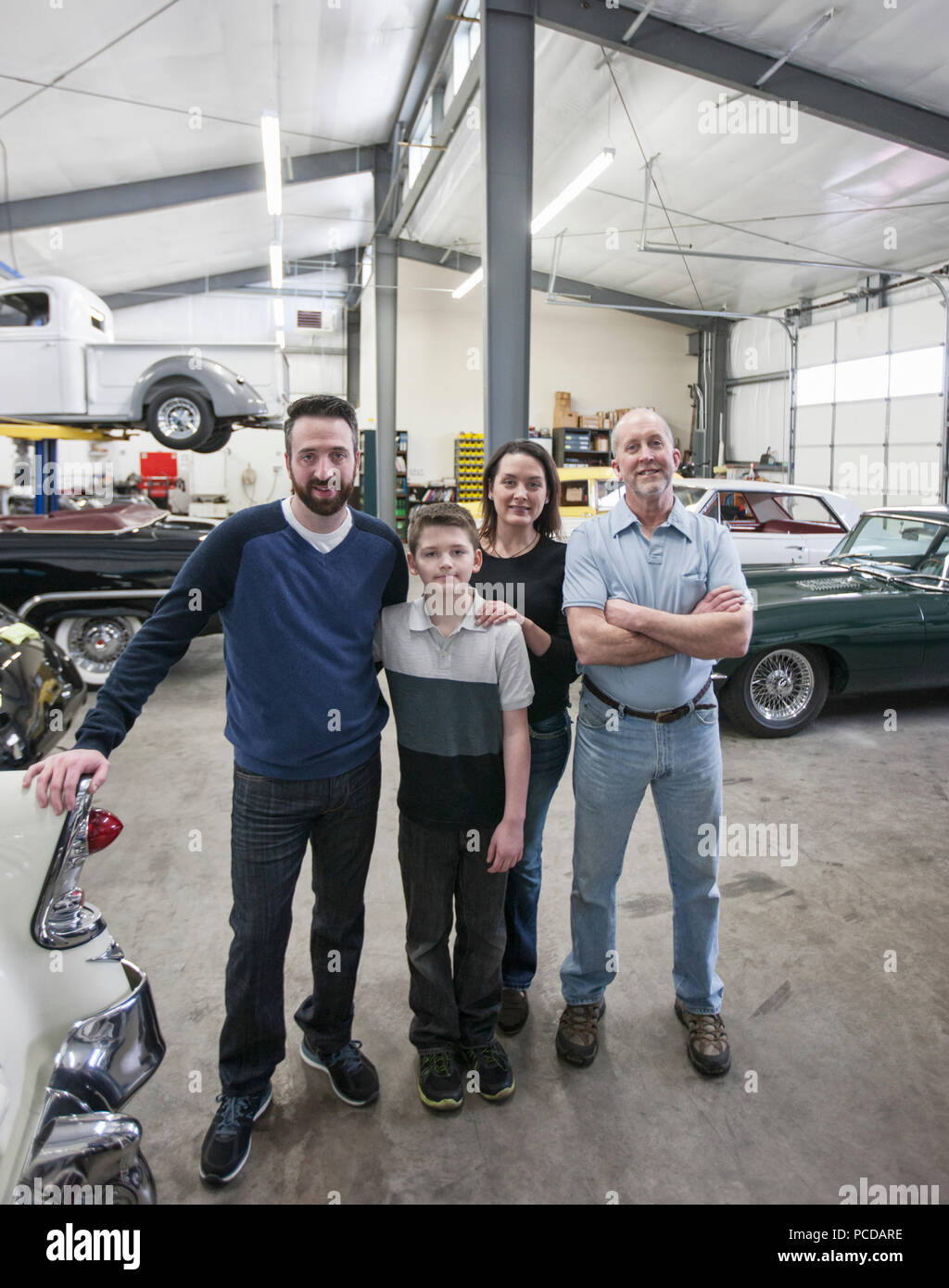 A family business, father, son and grandson, and a young woman posing in a classic car repair shop. Stock Photo