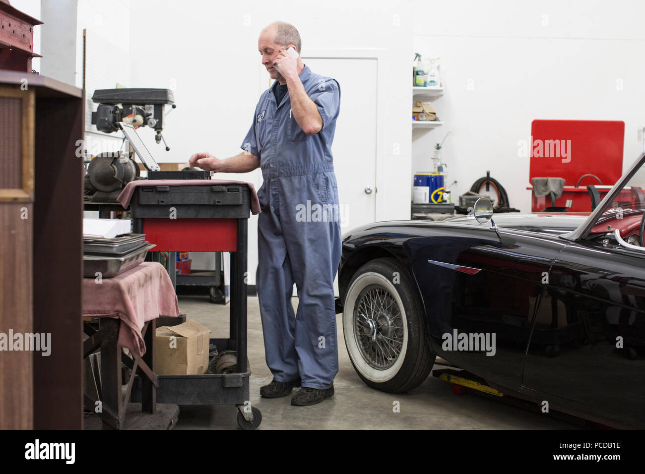 A senior caucasian male car mechanic working on his laptop computer in