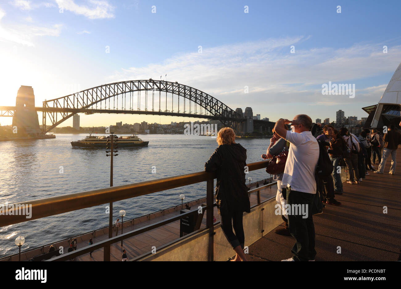 People watching the sun set behind Sydney Harbour Bridge, from the terrace outside the Opera House, Sydney, NSW, Australia Stock Photo
