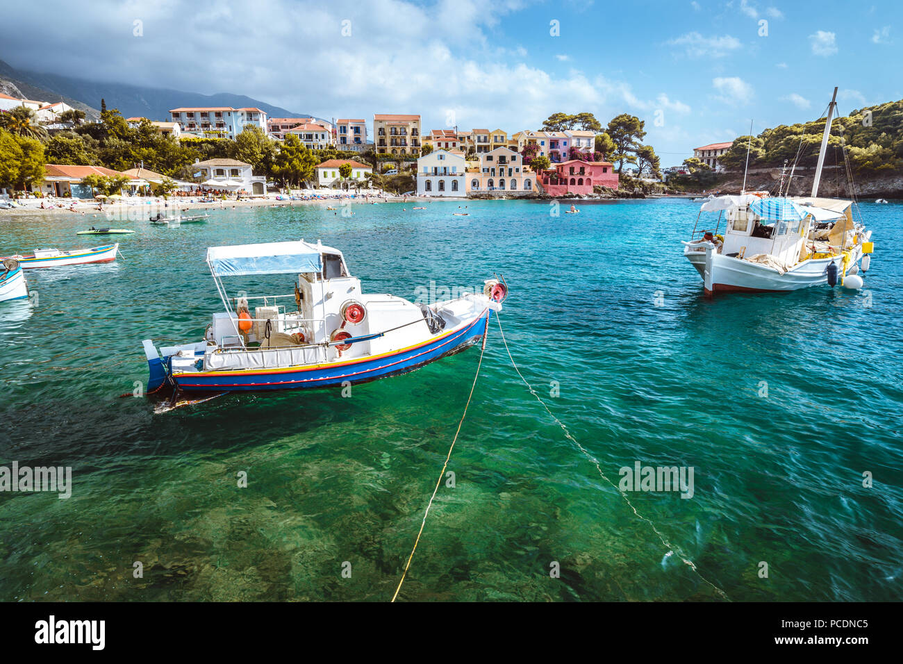 Assos village on Kefalonia island, Greece. White blue local boats at anchor in the emerald rippled sea water bay. Stock Photo