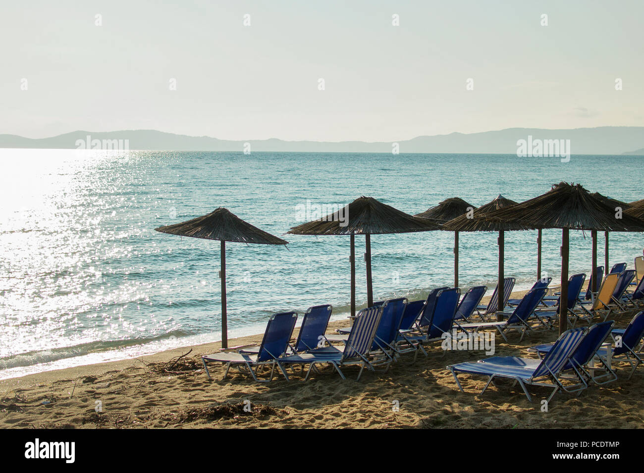 Morning at a beach with loungers under palm tree leaves umbrellas. Ierissos, Greece. Stock Photo