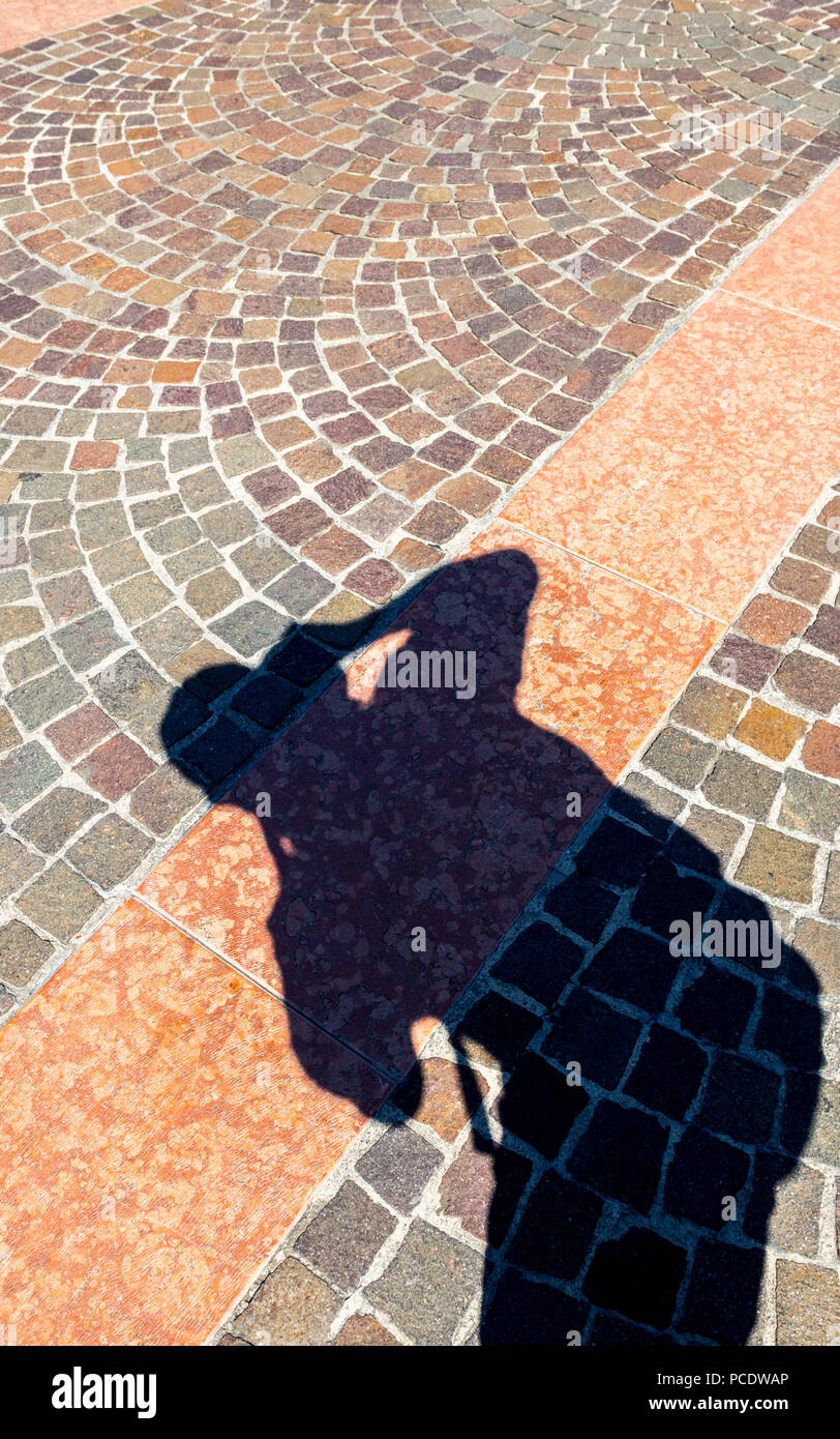 Shadow of a photographer taking an image of the patterned cobble stones  at an Italian piazzetta. Stock Photo