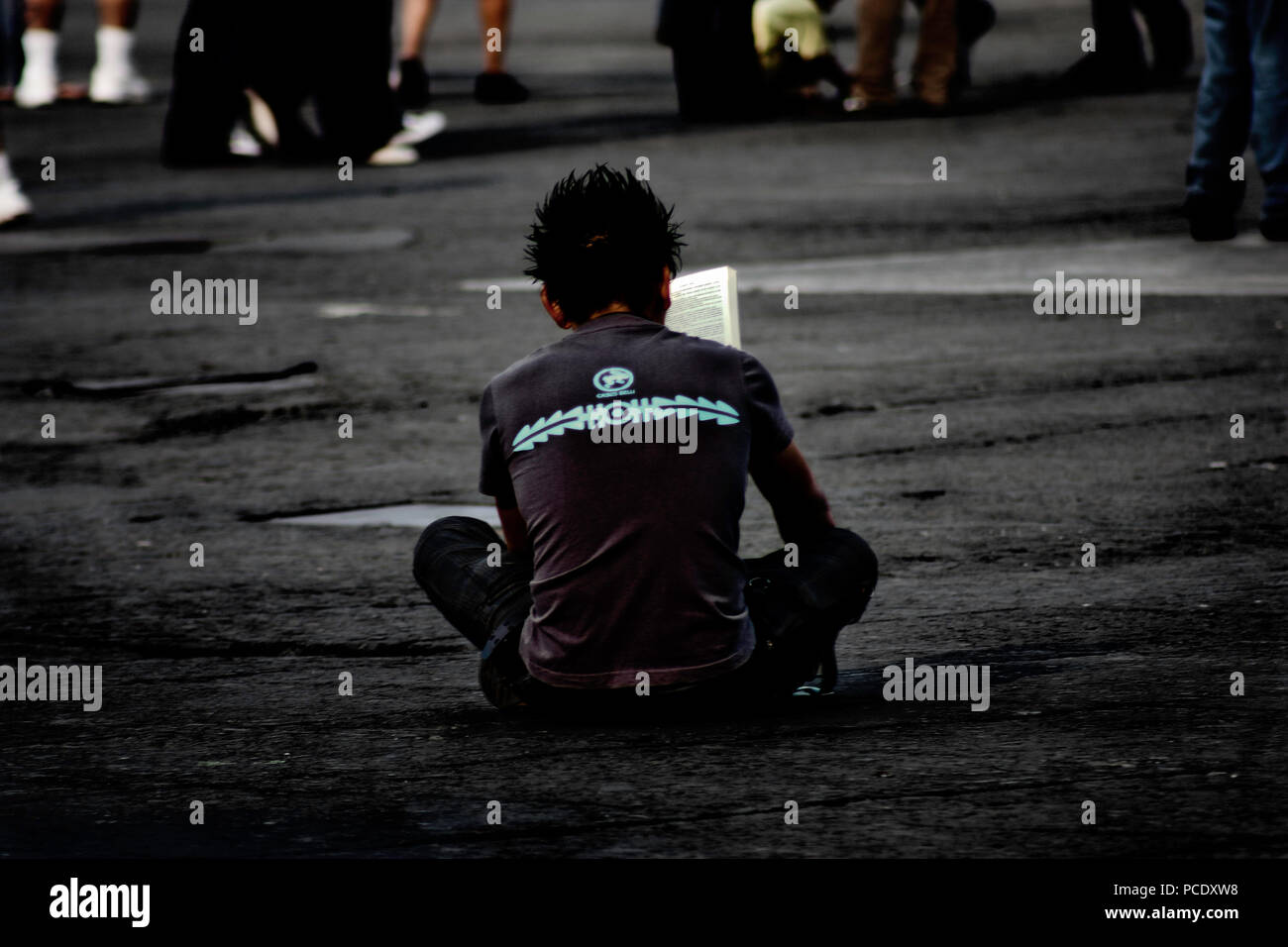 A boy sitting in the middle of the Mexico square reading while people walked around him. Stock Photo