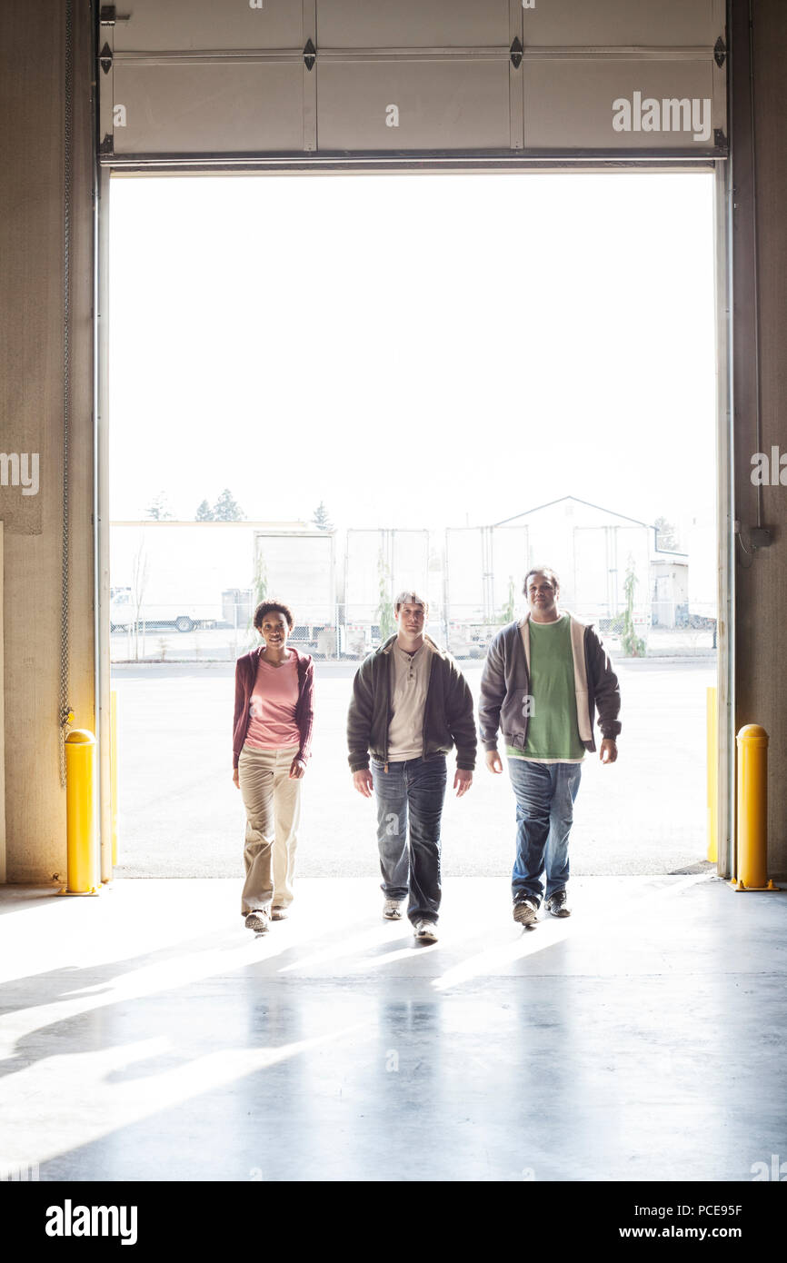 Three employees walking through the loading dock door of a distribution warehouse. Stock Photo