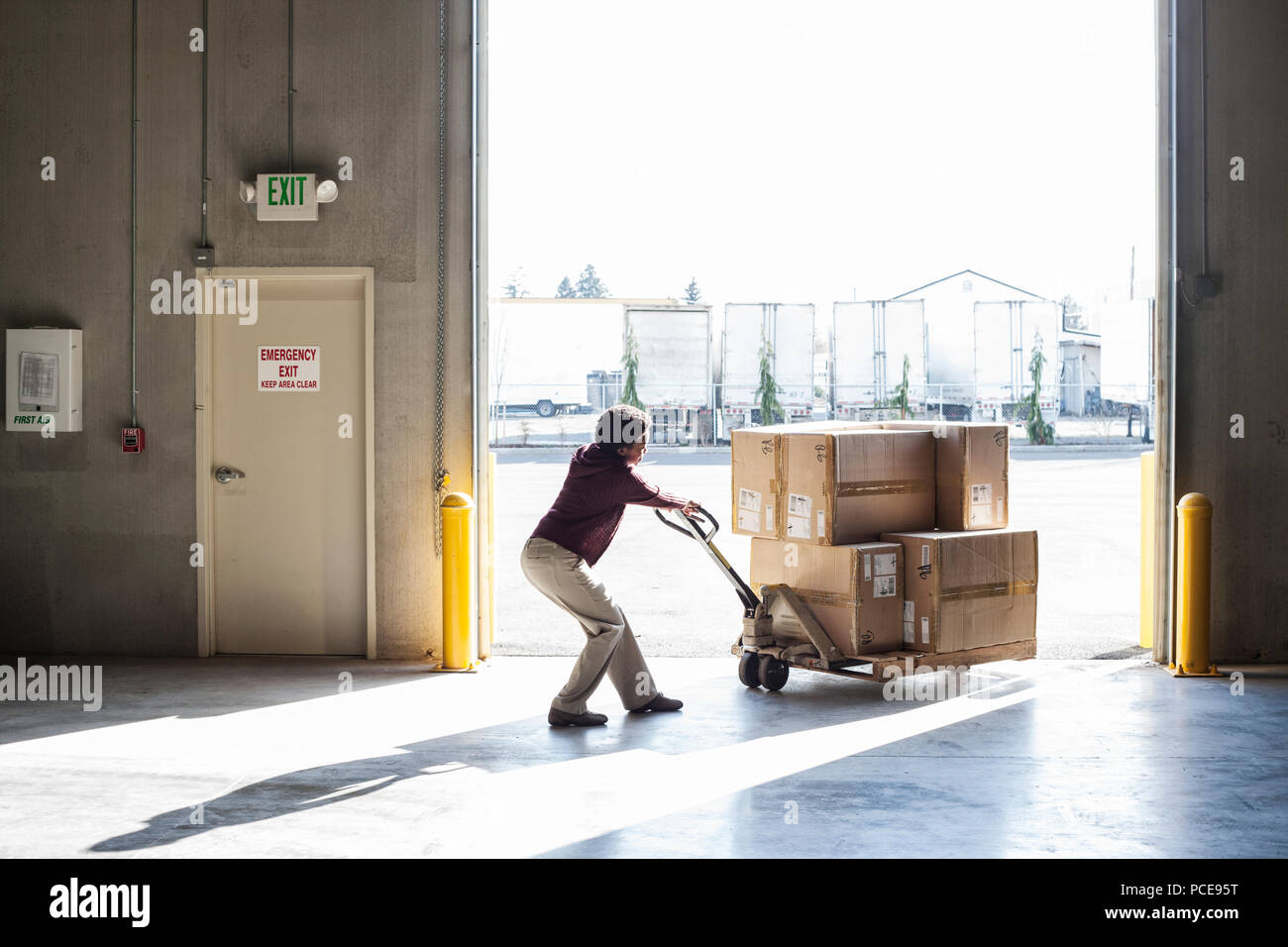 A female warehouse worker moving products in cardboard boxes by using a ...