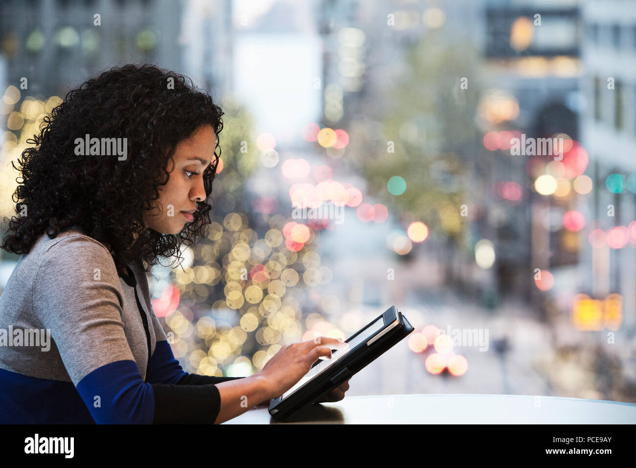 A view of a black businesswoman working on a notebook computer in front of an office window looking out on a city street scene just before dark. Stock Photo