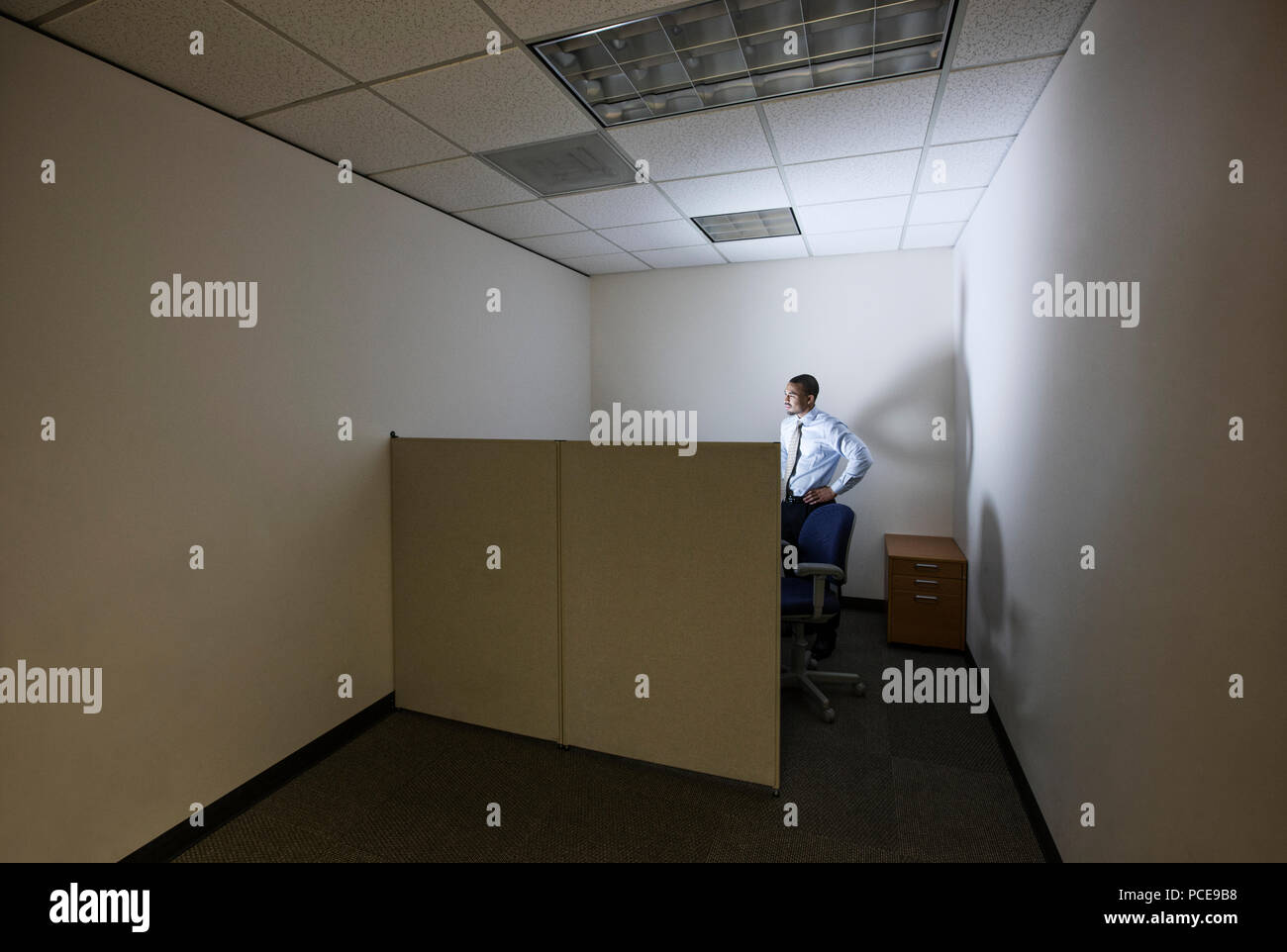 A businessman lit up by a computer screen in his small corner office ...