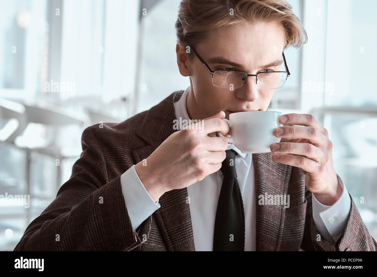Young businessman in eyeglasses at office sitting drinking coffe Stock Photo
