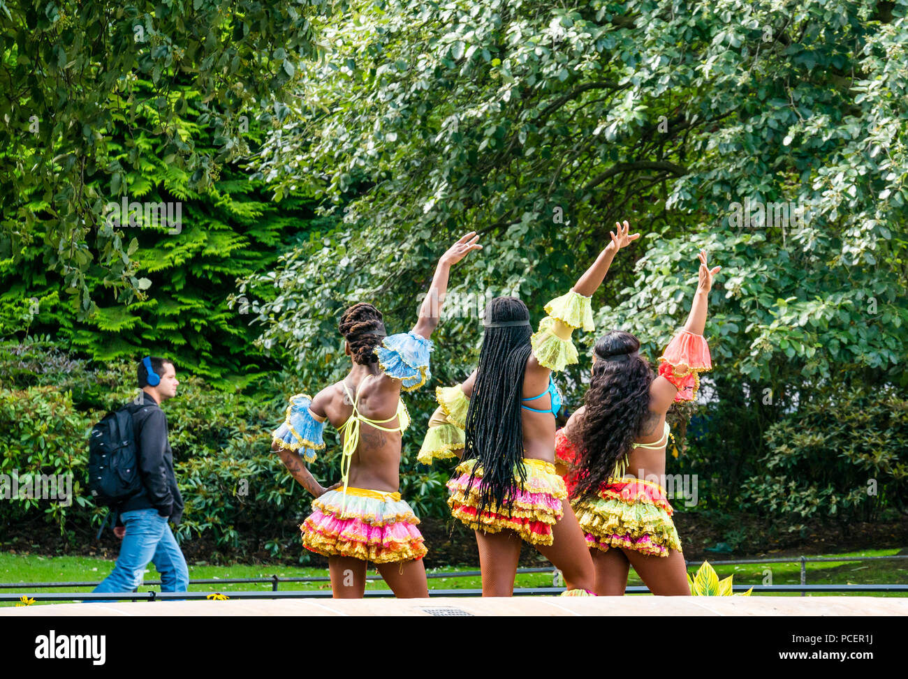 Photocall Caribbean Dynasty dancers of UniverSoul Circus, Princes Street Gardens, Edinburgh, Scotland, UK during Fringe Festival with man walking by Stock Photo