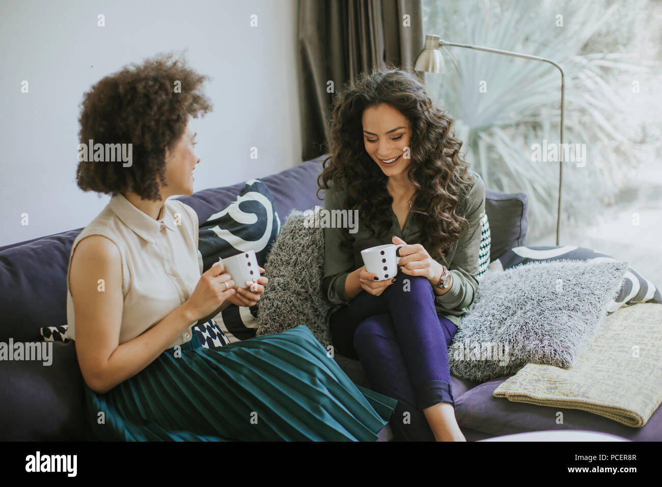 Two multiracial young women chatting and drinking coffe in rhe living room Stock Photo