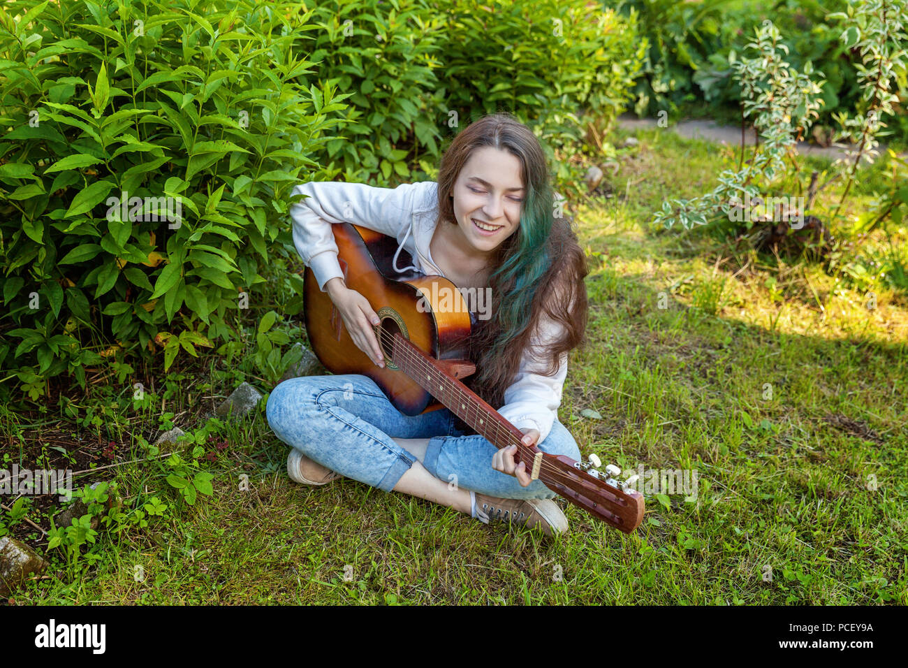 Young hipster woman sitting in grass and playing guitar on park or ...