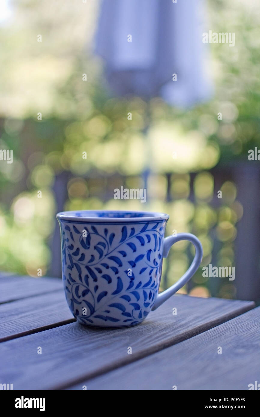 Mug in blue pattern on wooden table outdoors in the shade in a garden. Stock Photo