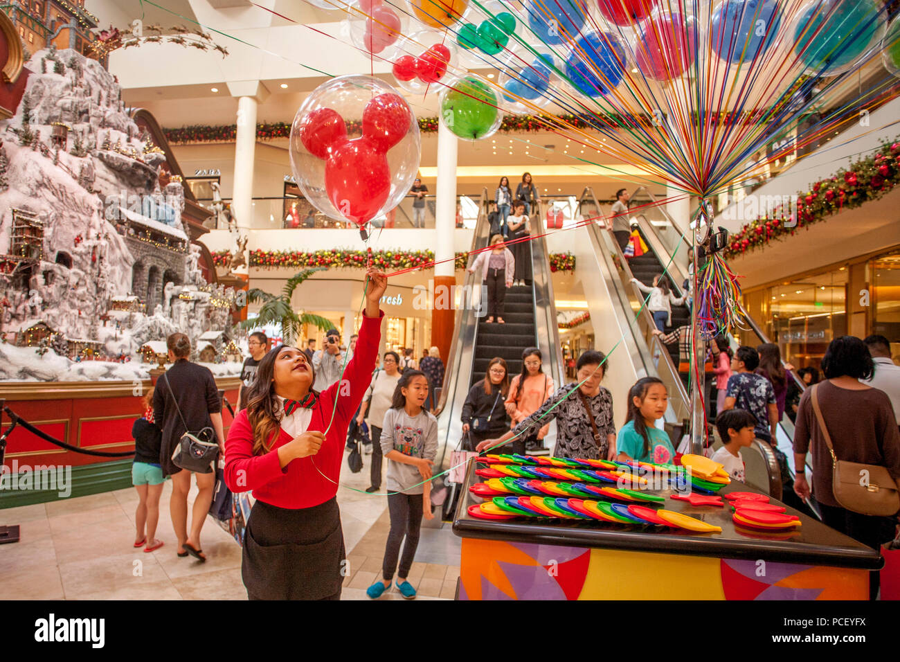 A shopping mall clerk welcomes Christmas shoppers with balloons in Costa  Mesa, CA. Note model of snow covered village at left Stock Photo - Alamy