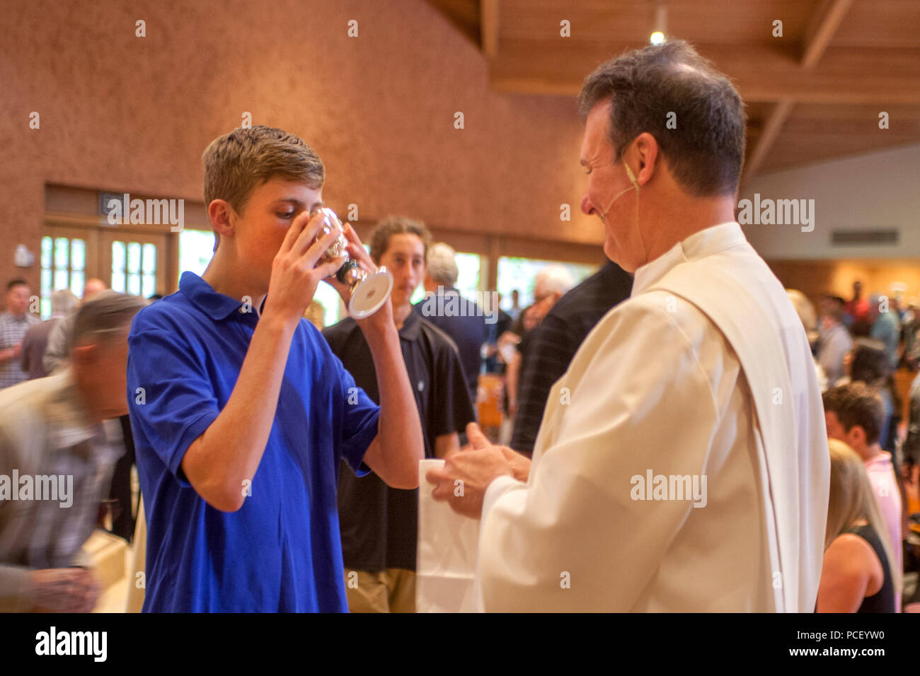 A robed deacon offers the communion cup to a male young adult