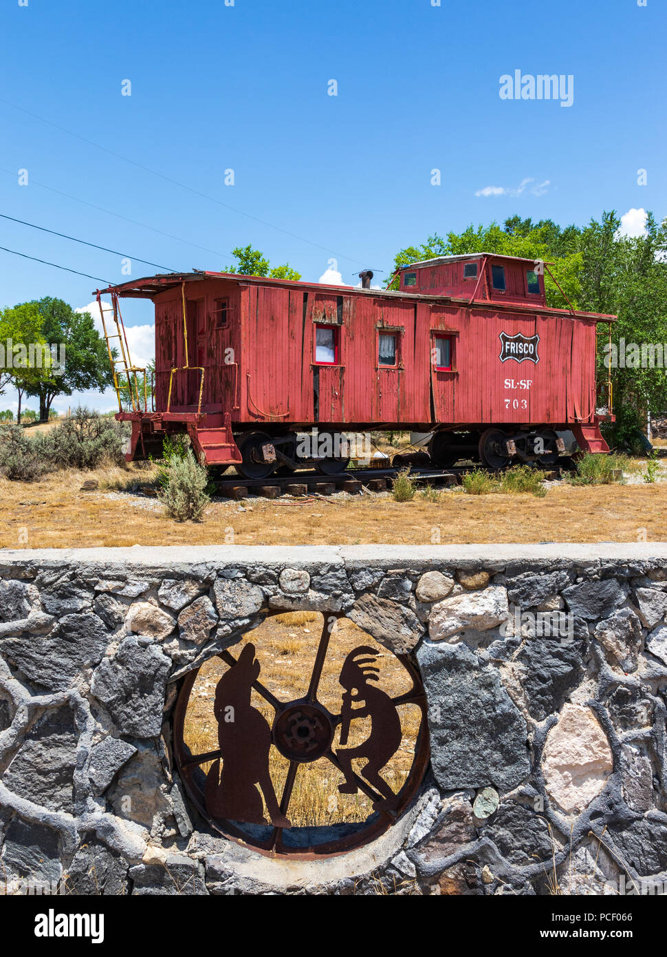 TAOS, NM, USA-12 JULY  18: A rock wall with iconic metal  figures of Kokopelli and Coyote imbedded into it, with a train caboose beyond. Stock Photo