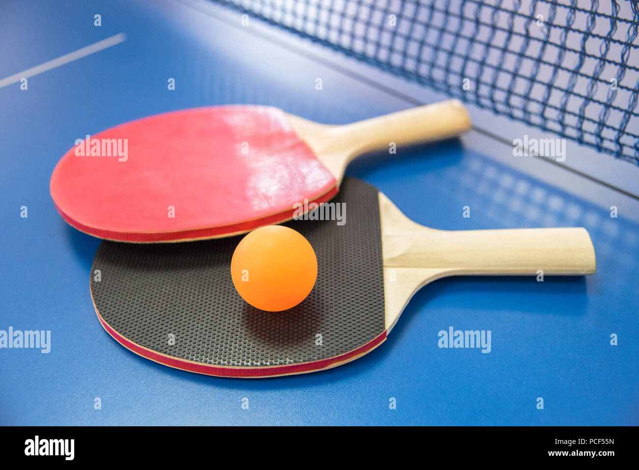 Orange ball for table tennis and two wooden rackets of red and black color on a blue table with a grid Stock Photo