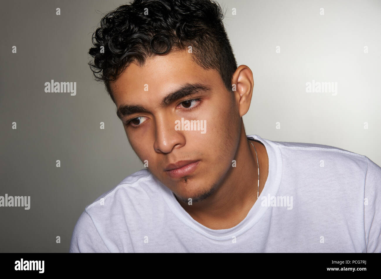 Studio portrait of a 19 years old young man, wearing a white t-shirt, looking down, to the side Stock Photo