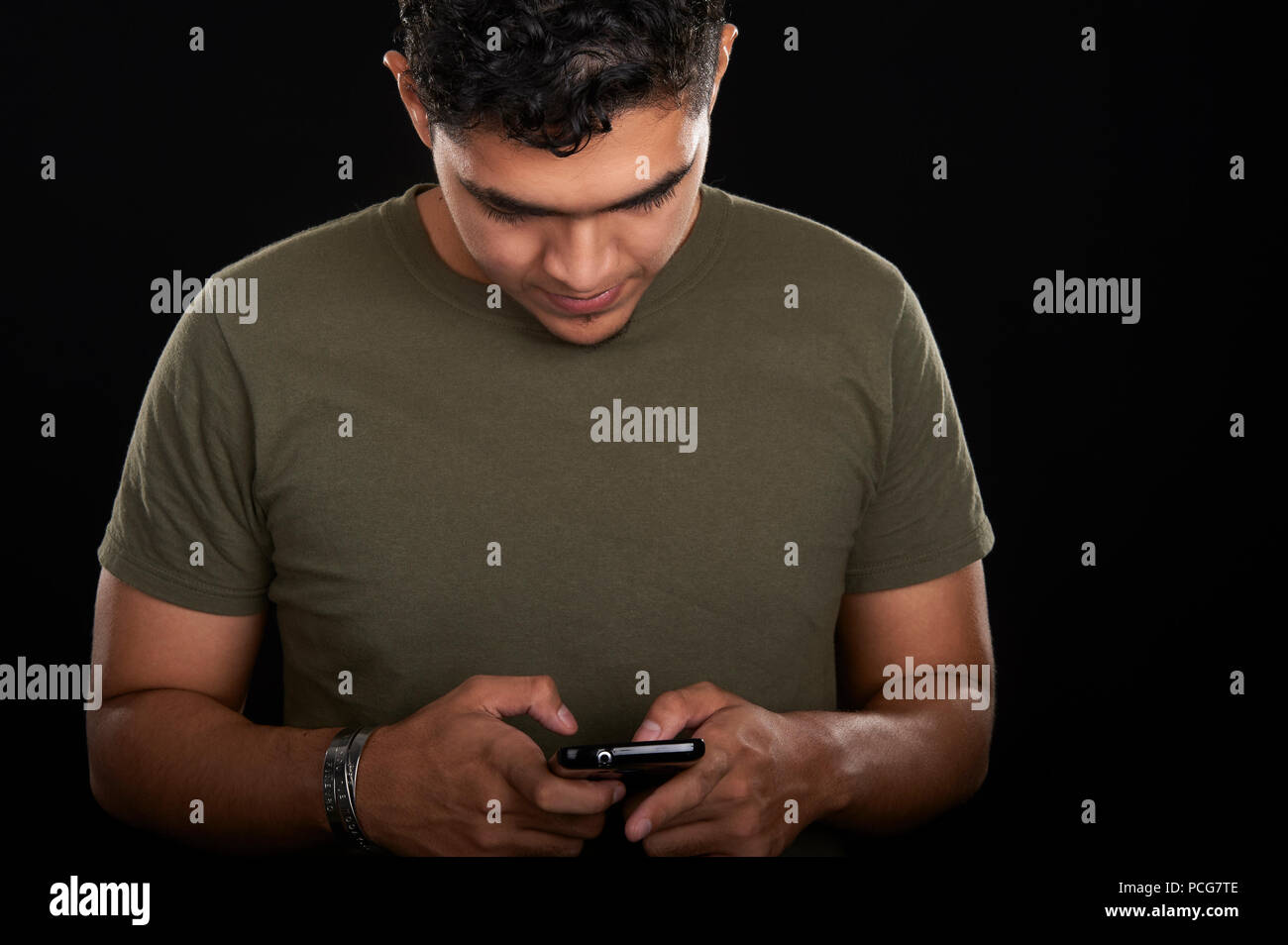 Studio portrait of a 19 years old young man, wearing an olive t-shirt, checking for messages on his smartphone Stock Photo