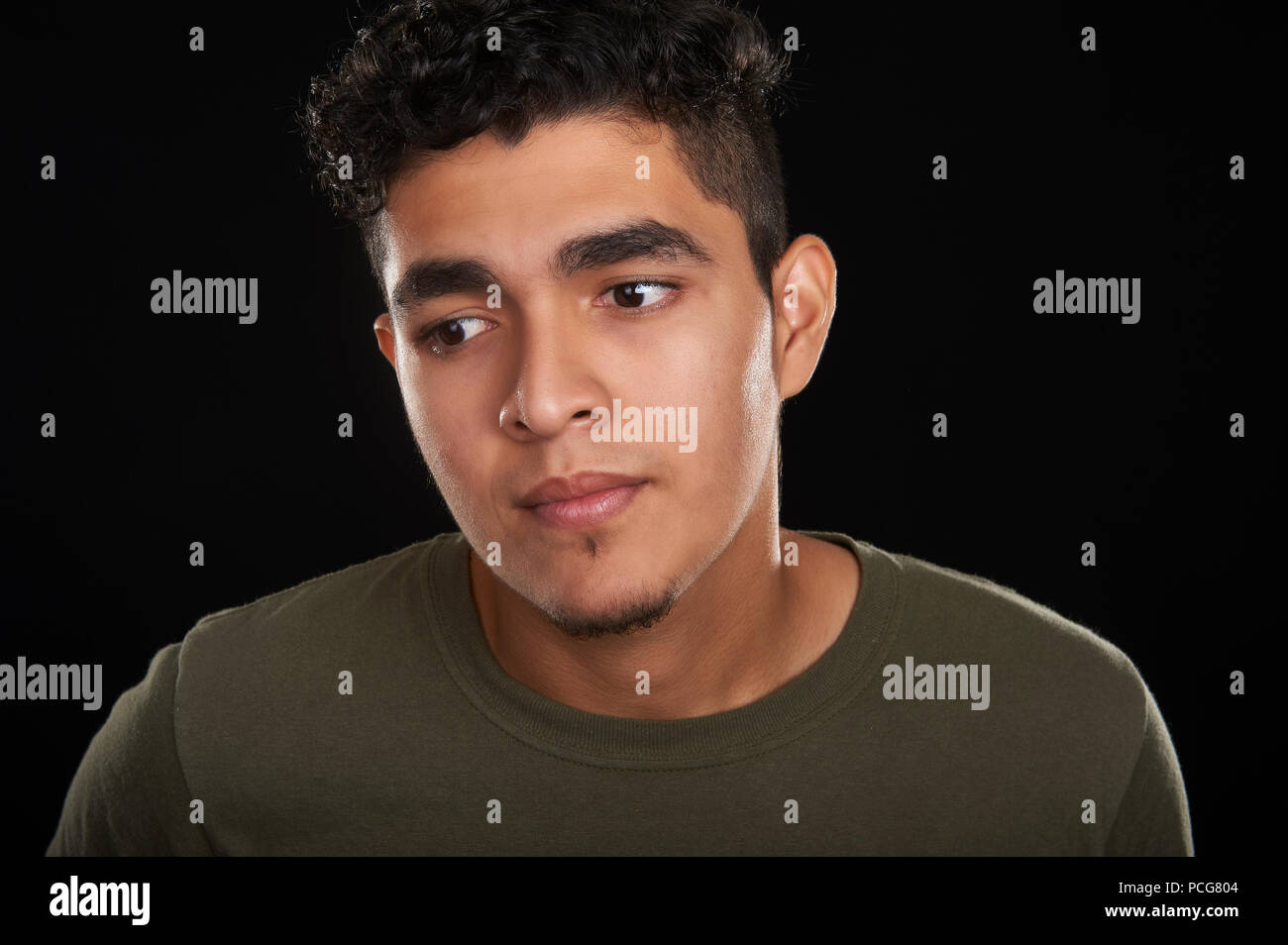 Studio portrait of a 19 years old young man in an olive t-shirt, looking down, to the side Stock Photo