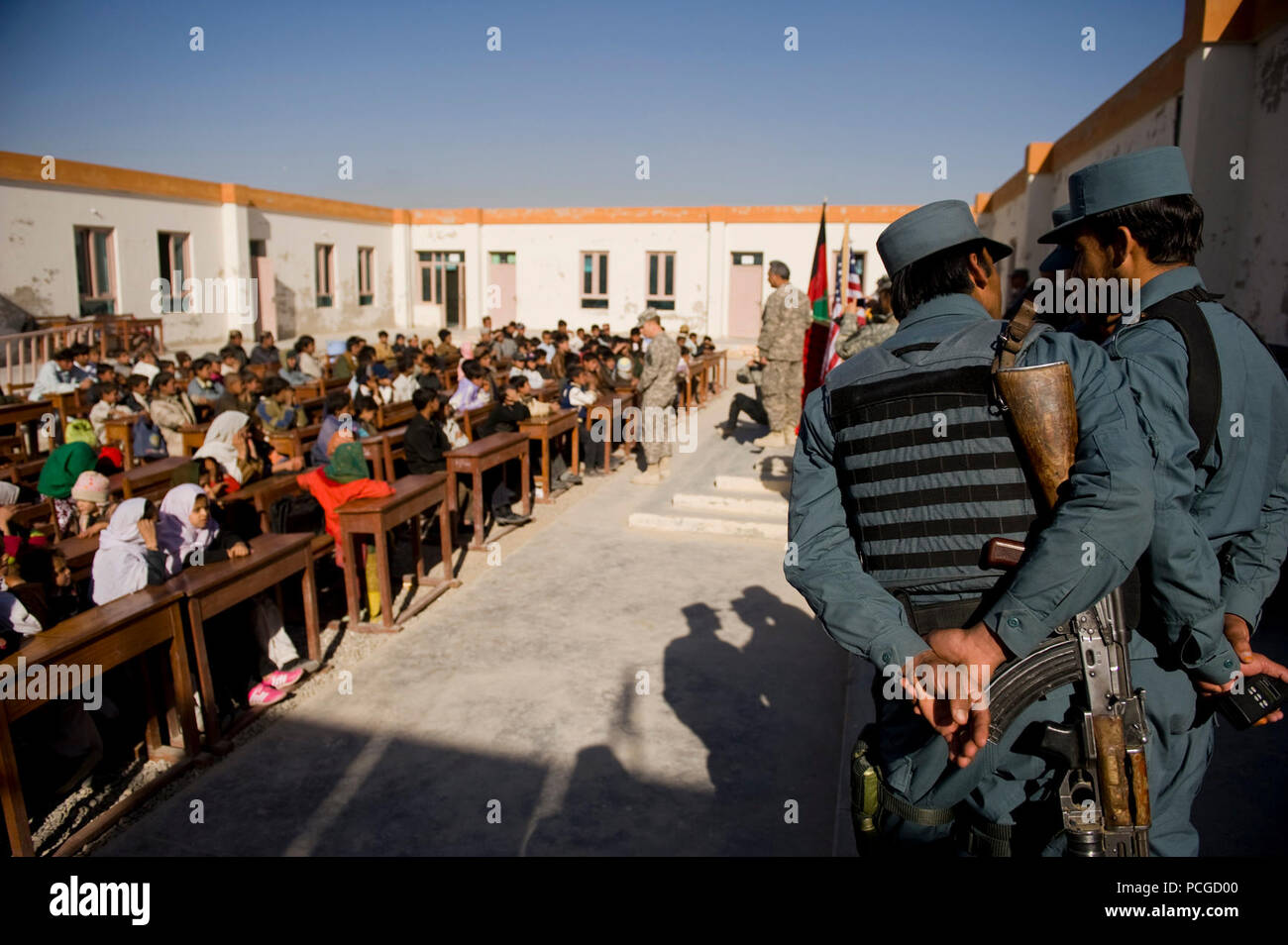Afghan national policemen look on as a local coalition leader speaks to children at an elementary school near Kandahar Air Field. Both Afghan and coalition leaders spoke to the children on the importance of education and good behavior before handing out school supplies. Stock Photo