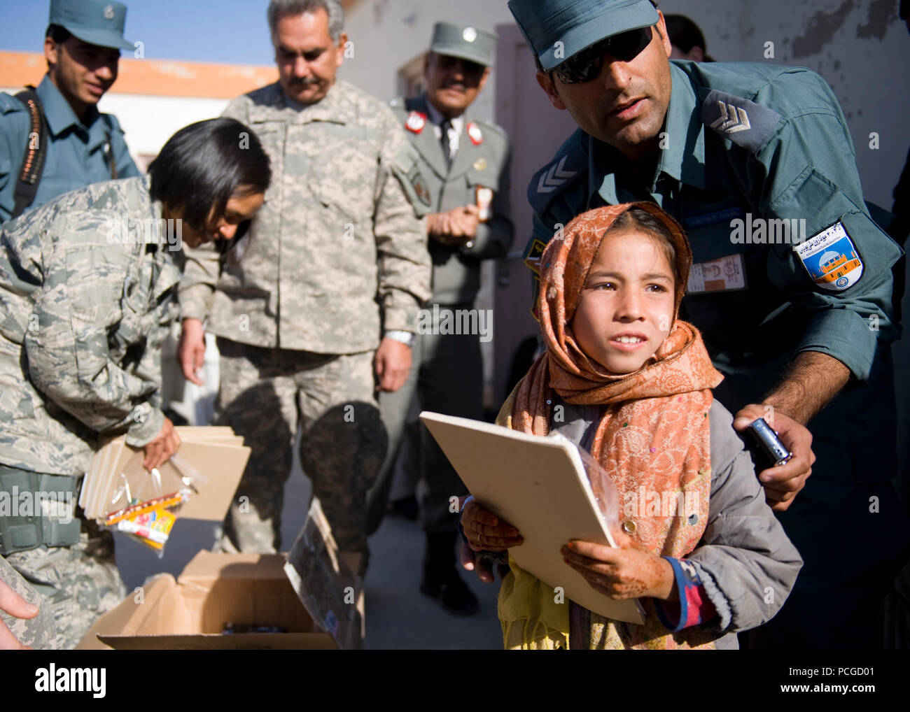 An Afghan girl receives school supplies from Afghan national policemen and coalition service members at an elementary school near Kandahar Air Field. During the visit, both Afghan and coalition leaders spoke to the children on the importance of education and good behavior before handing out school supplies. Stock Photo