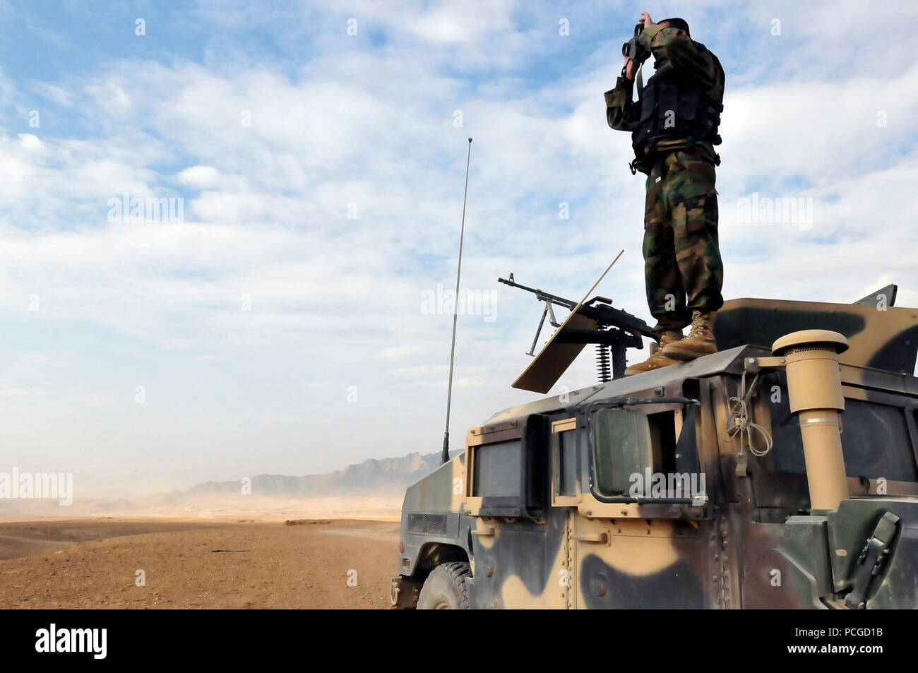 An Afghan National Army soldier stands atop his Humvee in the early morning providing security for fellow soldiers during training on a live fire range. The security is also for the protection of civilians who surround the range in order to prevent anyone from accidentally walking on to the range during hazardous training. Stock Photo