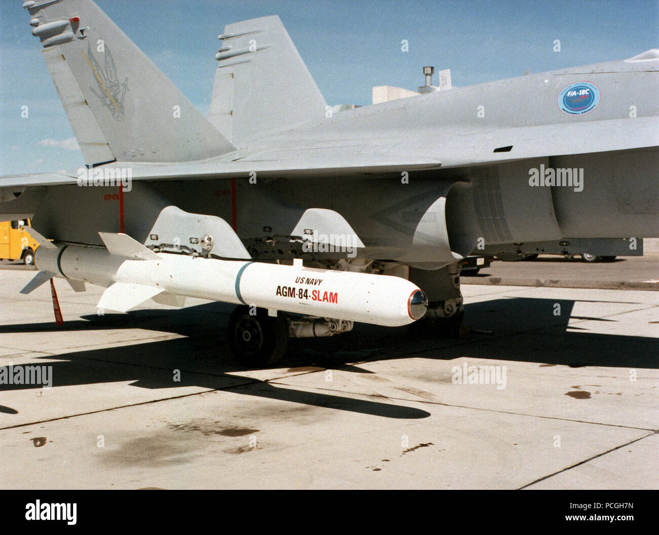 A view of an AGM-84 Harpoon air-to-surface anti-ship missile fixed under the wing of an F/A-18C Hornet aircraft parked on a flight line. Stock Photo