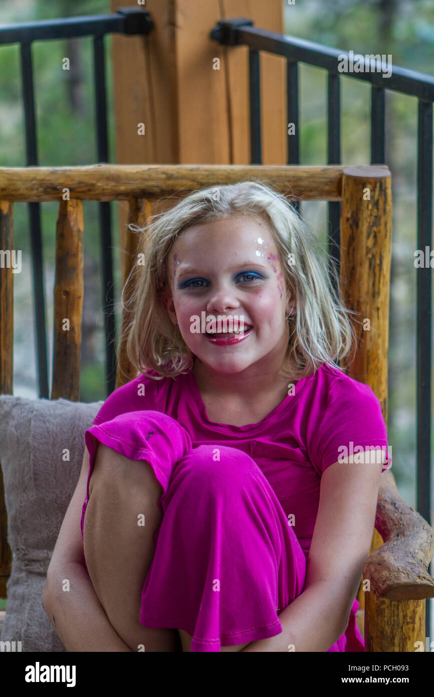 Young blonde, with excess make up, in pink dress, smilimg and looking at camera, hugging knees. Moel r elease # 113 Stock Photo