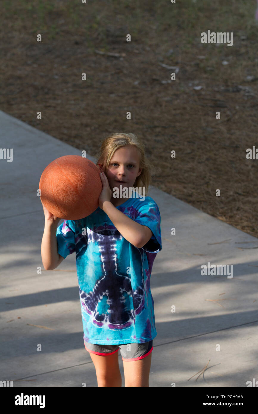 Pretty 8  year old female playing outdoor. basketball, wearing t-shirt and shorts. Model Relese #113 Stock Photo