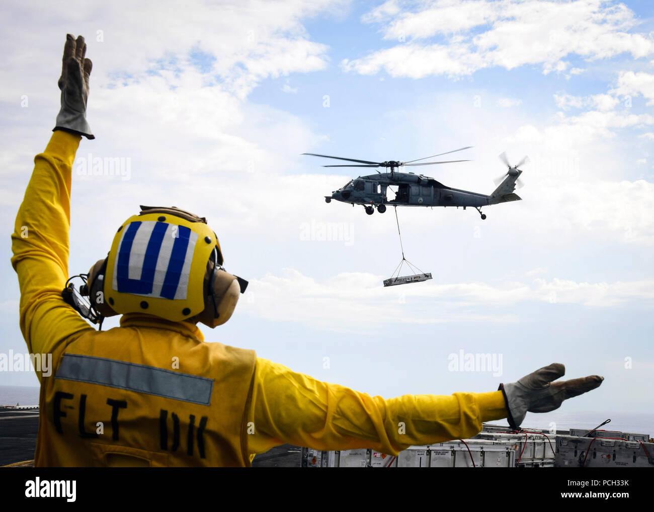 PACIFIC OCEAN (Oct. 24, 2016) A Sailor assigned to USS Nimitz (CVN 68) directs an MH-60S Sea Hawk from the Eightballers of Helicopter Sea Combat Squadron (HSC) 8 during an at-sea ammunition onload with the dry cargo/ammunition ship USNS Wally Schirra (T-AKE 8). Nimitz is underway conducting an ordnance-handling evolution in preparation for an upcoming 2017 deployment. Stock Photo