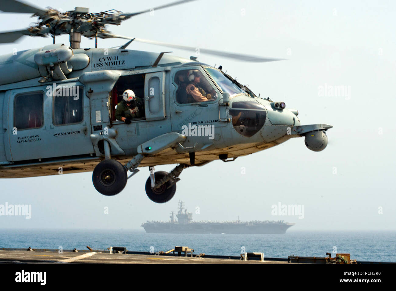 GULF OF OMAN (July 21, 2013) An MH-60S Sea Hawk helicopter from the Indians of Helicopter Sea Combat Squadron (HSC) 6 lands on the flight deck of the amphibious dock landing ship USS Carter Hall (LSD 50) while the aircraft carrier USS Nimitz (CVN 68) transits nearby. Carter Hall is part of the Kearsarge Amphibious Ready Group and, with the embarked 26th Marine Expeditionary Unit, is deployed in support of maritime security operations and theater security cooperation efforts in the U.S. 5th Fleet area of responsibility. Stock Photo