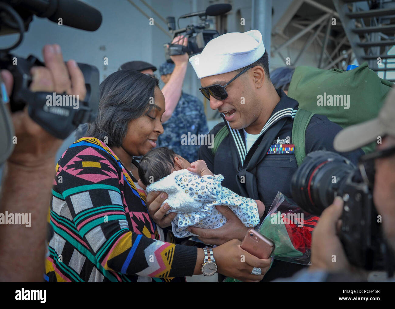 DIEGO (Feb. 2, 2018) Operations Specialist 2nd Class Jesse Soto  holds his newborn child for the first time during the homecoming of the amphibious assault ship USS America (LHA 6). America, part of the America Amphibious Ready Group, with embarked 15th Marine Expeditionary Unit (MEU), is returning from a regularly scheduled deployment to the Western Pacific and Middle East. The U.S. Navy has patrolled the Indo-Pacific region routinely for more than 70 years promoting peace and security. Stock Photo