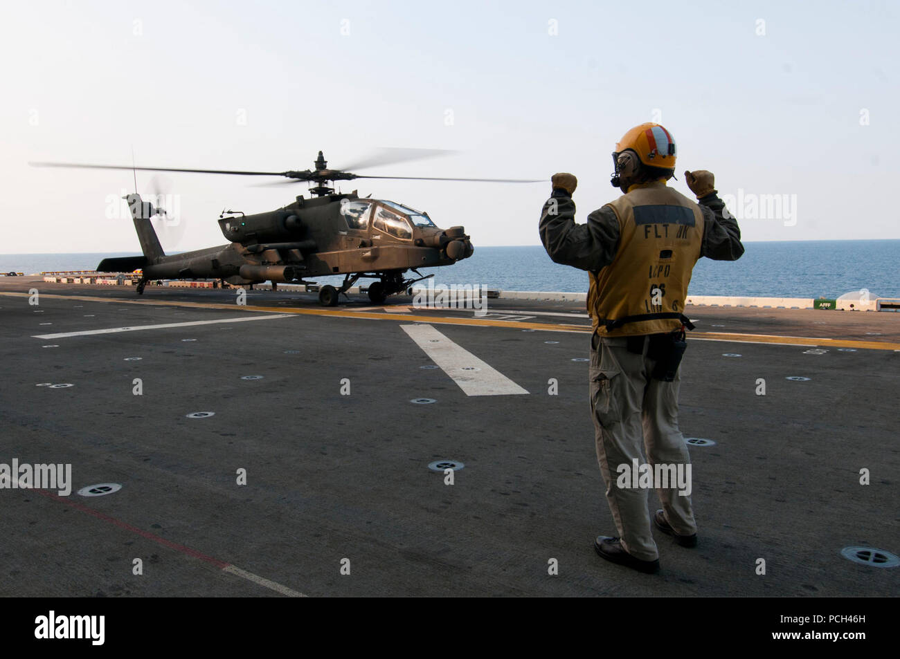 A U.S. Sailor directs the pilots of an Army AH-64D Apache Longbow helicopter assigned to the 4th Aerial Reconnaissance Battalion, 2nd Combat Aviation Brigade, 2nd Infantry Division to land aboard the amphibious assault ship USS Bonhomme Richard (LHD 6) in the East China Sea April 11, 2014. The Bonhomme Richard was underway in the U.S. 7th Fleet area of responsibility supporting maritime security operations and theater security cooperation efforts. Stock Photo