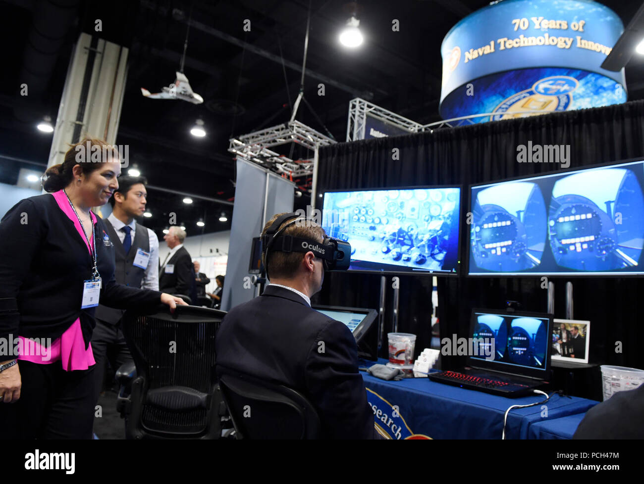 NATIONAL HARBOR, Md. (May 16, 2016) Lauren Burnette, from Space and Naval Warfare Systems Command (SPAWAR) Systems Center Pacific, explains the Battlespace Exploitation of Mixed Reality (BEMR) Lab demo to a visitor at the Office of Naval Research (ONR) exhibit during the 2016 Sea-Air-Space Exposition. BEMR is designed to showcase and demonstrate cutting edge low cost commercial mixed reality, virtual reality and augmented reality technologies and to provide a facility where warfighters, researchers, government, industry and academia can collaborate. Stock Photo