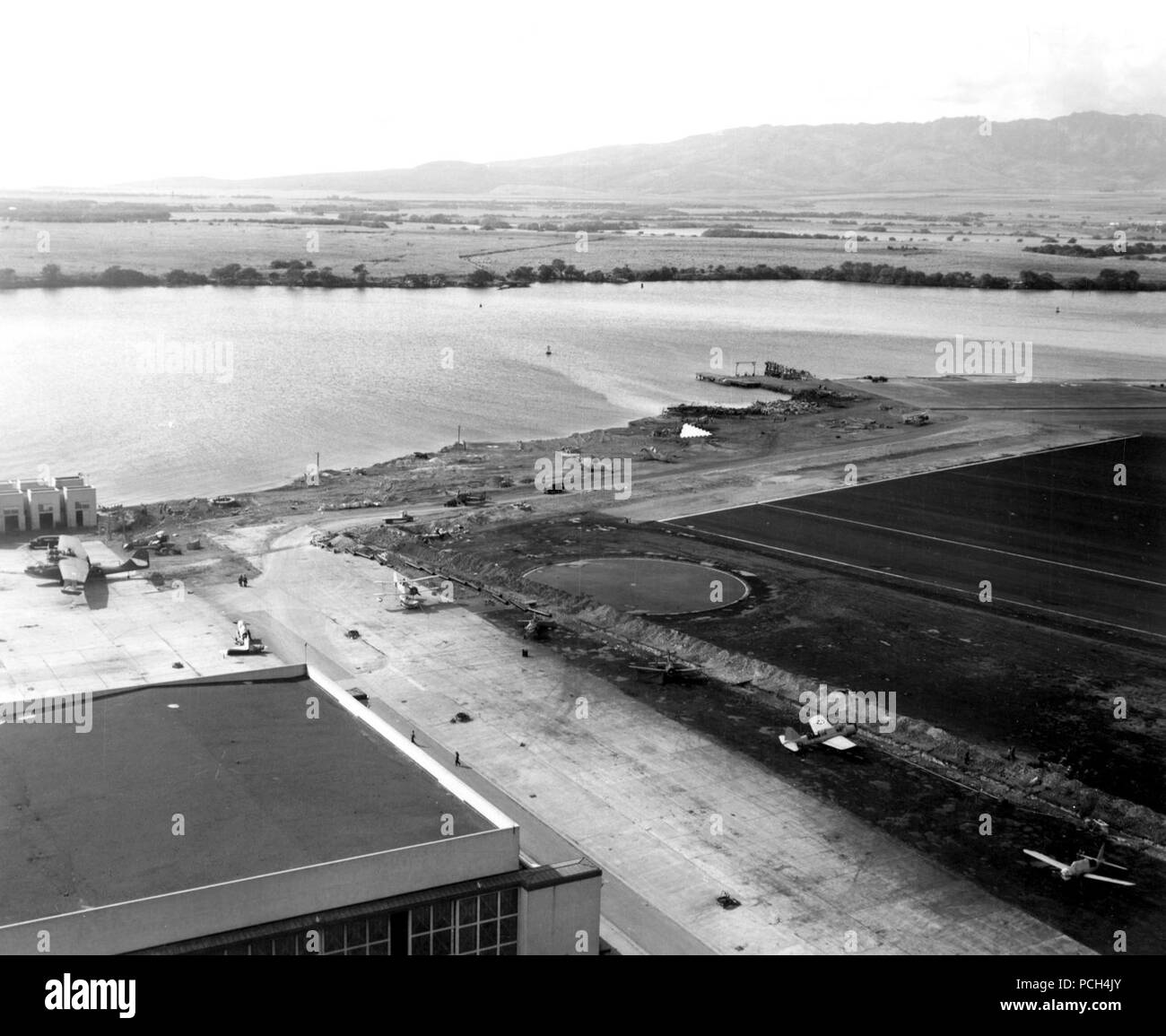 View looking toward the southern end of Ford Island on 8 December 1941, the day after the Japanese raid on Pearl Harbor. Planes present include at least seven OS2U, two SOC, one PBY-5, one F4F-3 and two TBD-1s. One of the TBDs may be Bureau # 0289, which was flown by Ensign Theodore W. Marshall, USNR, during his attempt to follow Japanese planes back to their carriers on 7 December. He was awarded the Silver Star for the effort. Stock Photo