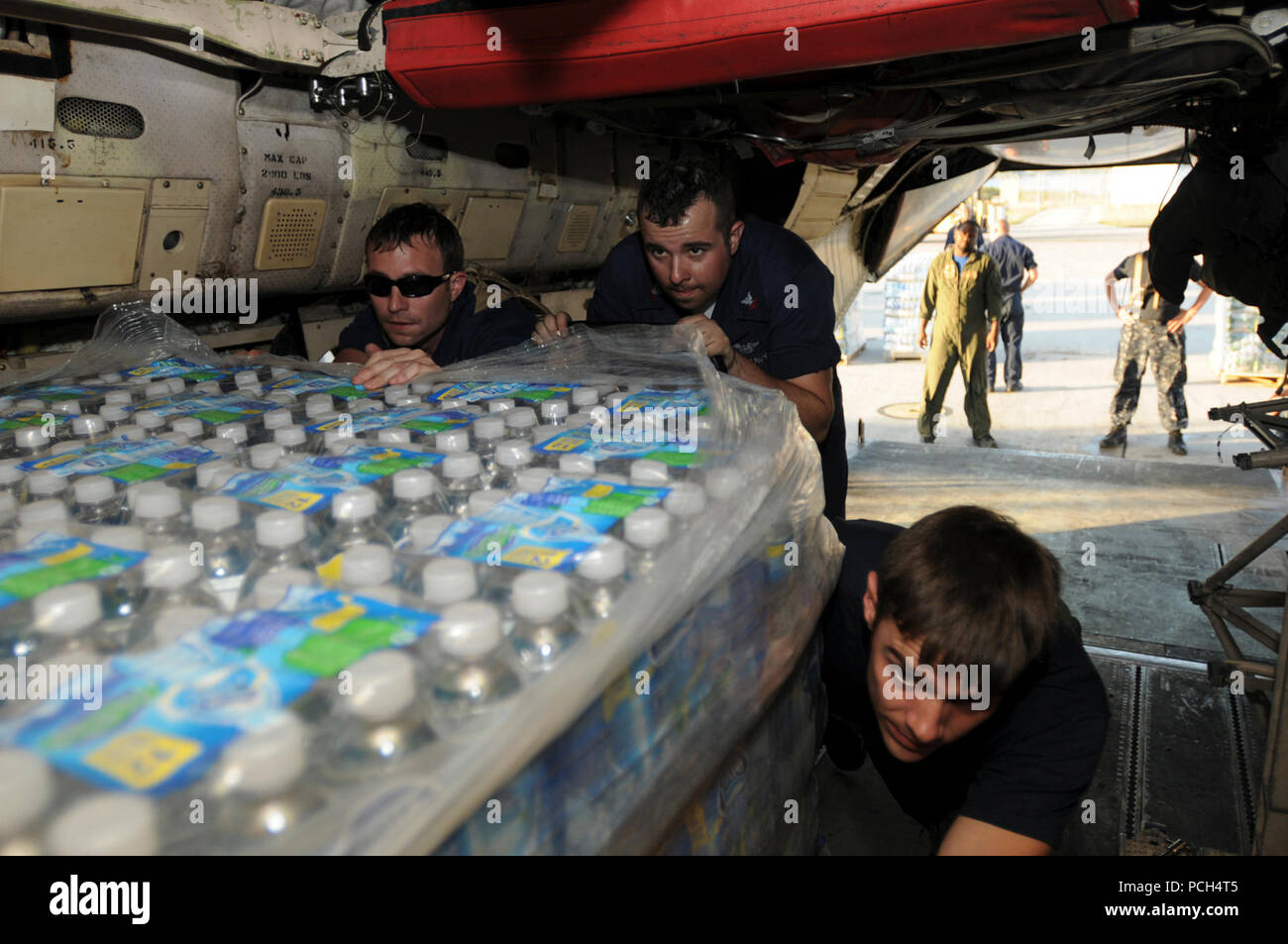 From left, Navy Petty Officers 2nd Class Donald Boylen, an aviation structural mechanic, Justin Leonard, an aviation electronics technician and Jamie Salmon, an aviation warfare flight crewman, push pallets of water onto a C-2 Greyhound aircraft at U.S. Naval Station Guantanamo Bay, Jan. 24. The pallets of water, scheduled for delivery to Haiti, are part of humanitarian assistance in support of Operation Unified Response. Stock Photo