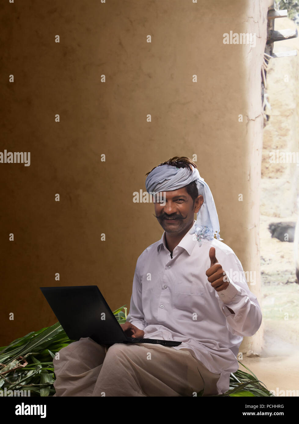 Rural farmer showing thumb up while working on laptop Stock Photo