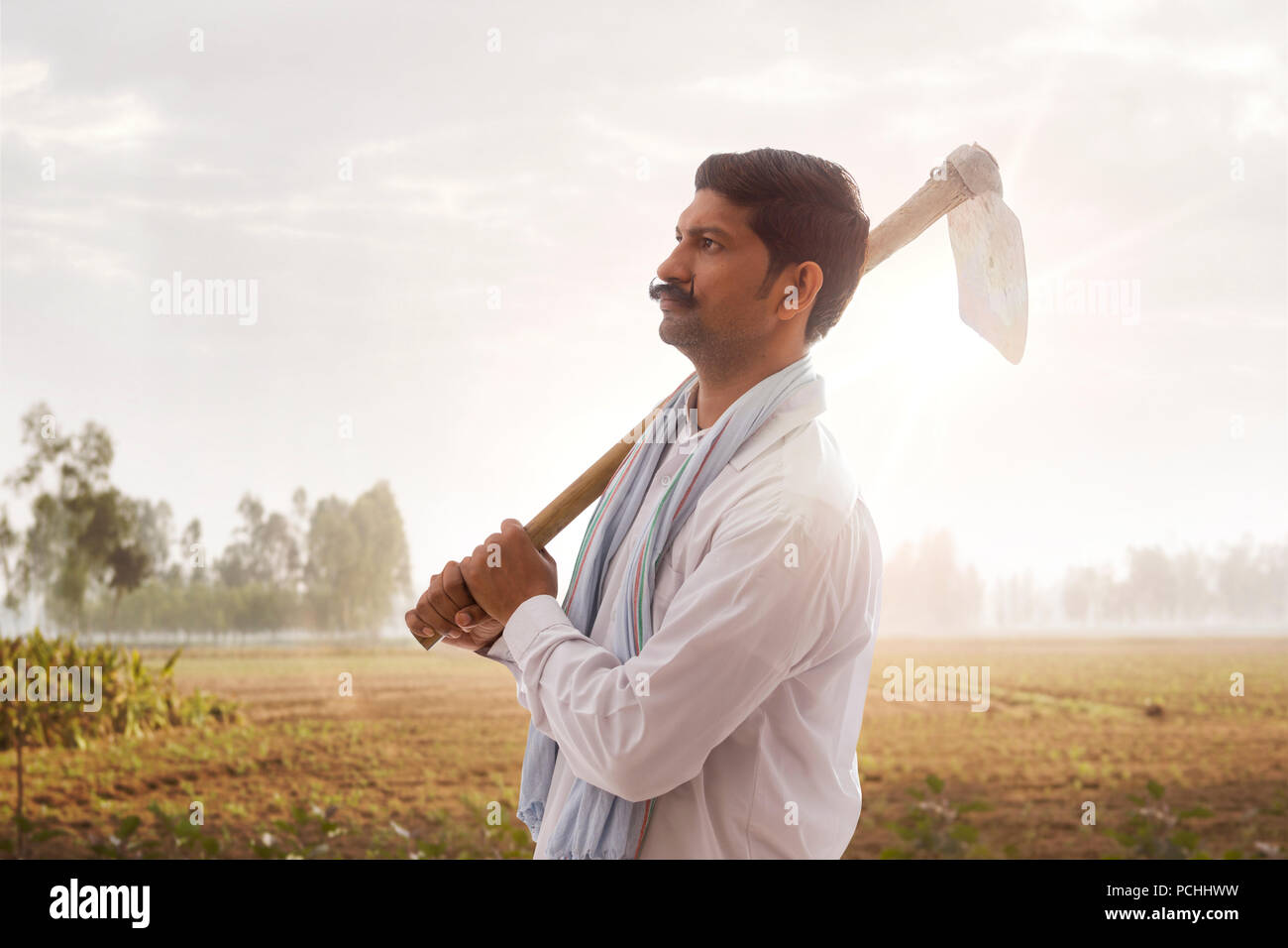 Indian farmer carrying hoe on his shoulder standing in field Stock Photo