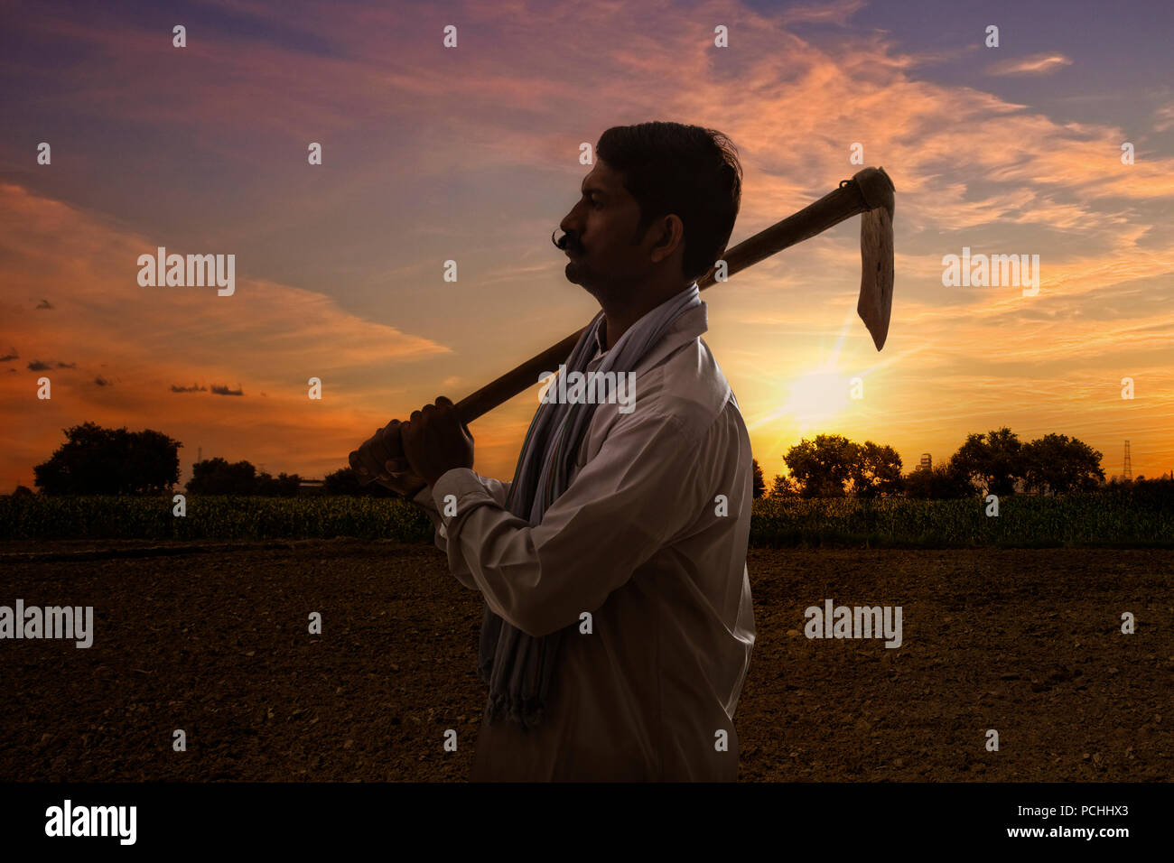 Indian farmer carrying hoe on his shoulder standing in field at sunrise Stock Photo