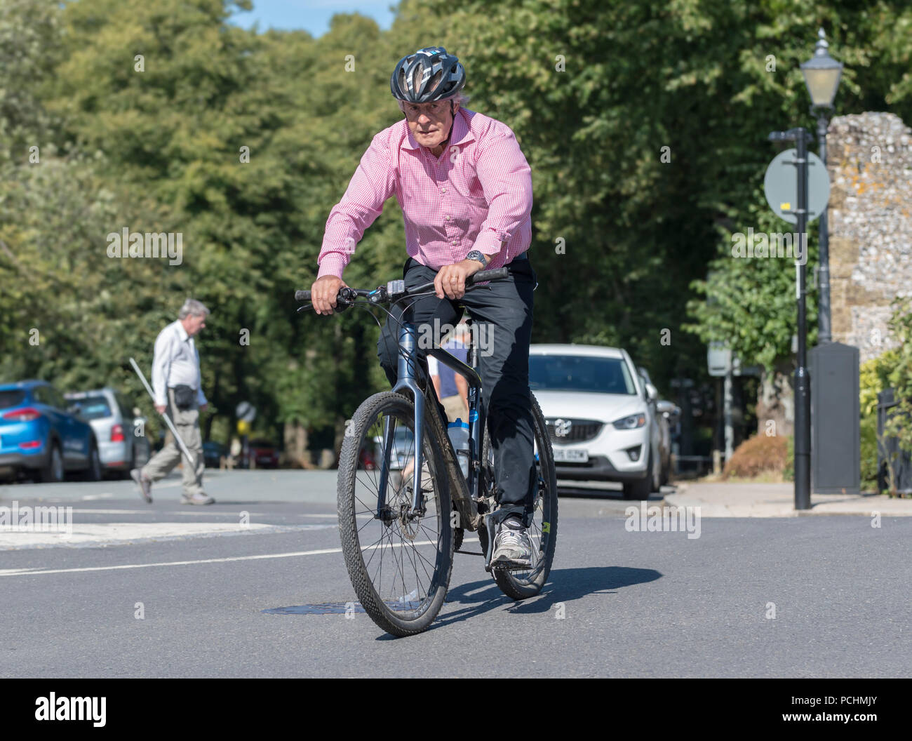 Middle aged man riding a bicycle in Summer in the UK. Middle aged cyclist on a British road. Stock Photo