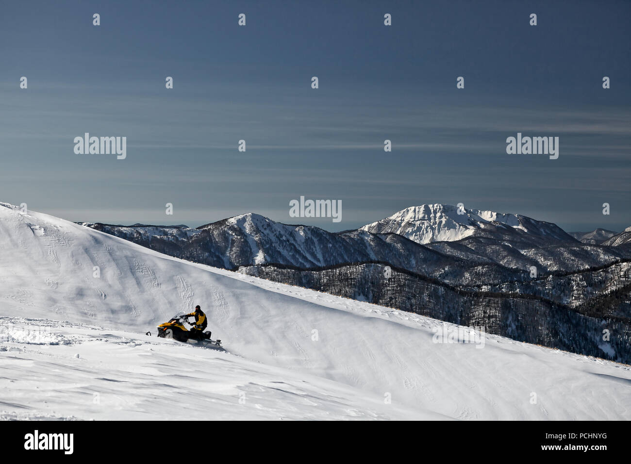 A man on a snowmobile races on snowy slope. State Nature Reserve in Adygea, Russia. Stock Photo