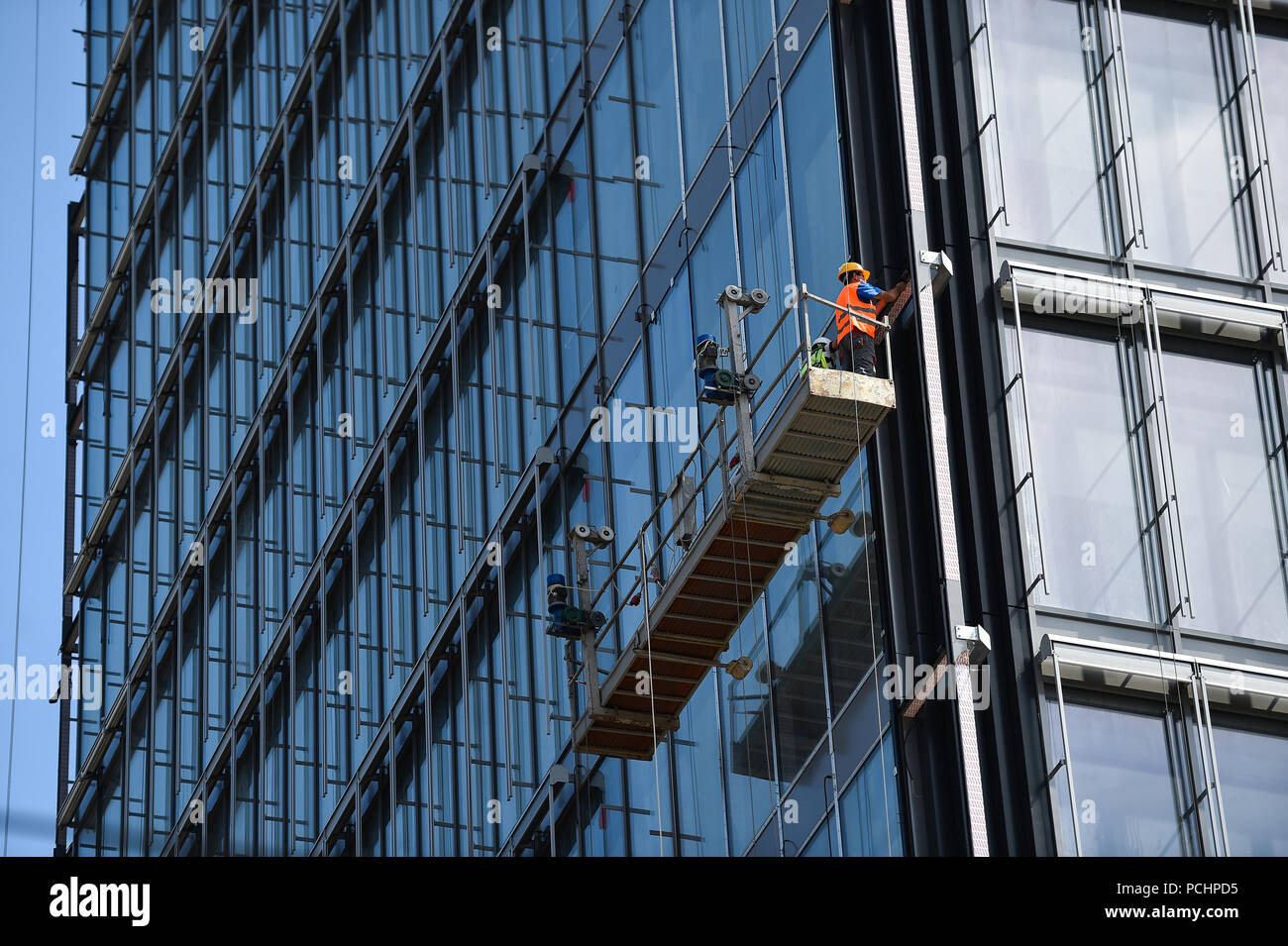 Construction workers on a suspended platform on a skyscraper glass facade Stock Photo
