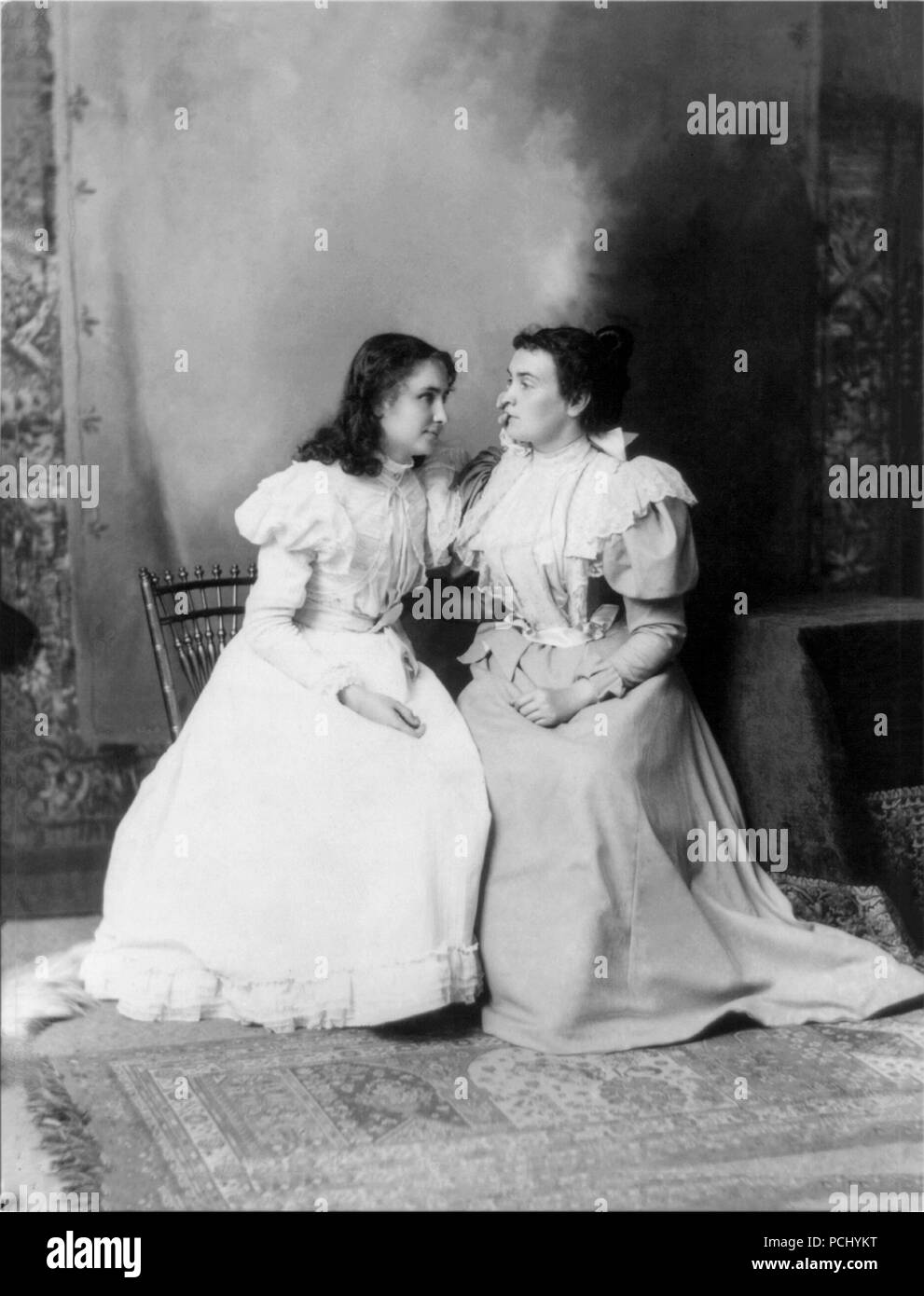 Helen Keller, seated with her teacher and companion Anne Sullivan in 1897 at an unknown location. Helen Keller (June 27, 1880 – June 1, 1968) was an American author, political activist, and lecturer. She was the first deaf-blind person to earn a bachelor of arts degree. Stock Photo