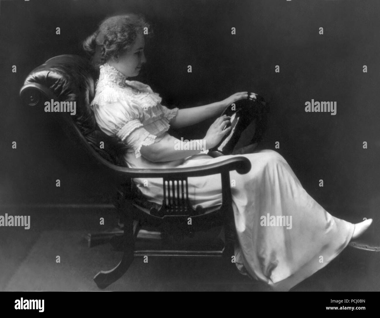 Helen Keller, full-length portrait sitting in a lounge chair holding a vase in left hand and touching it with her right hand in 1909. Helen Keller (June 27, 1880 – June 1, 1968) was an American author, political activist, and lecturer. She was the first deaf-blind person to earn a bachelor of arts degree. Stock Photo
