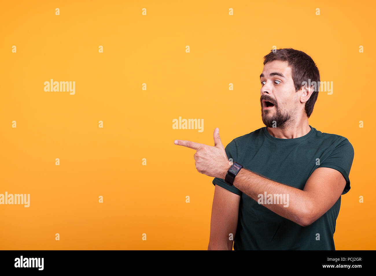 Expressive shocked man pointing at his right with his mouth open on orange background. Surprised guy pointing at the copyspace which is available for your advertising or promotions Stock Photo