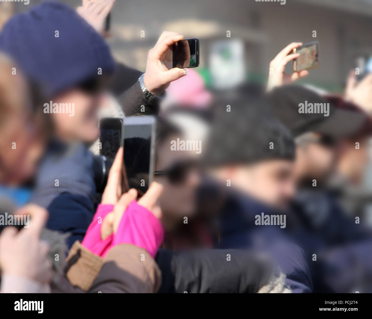A blurred crowd of people use different types of smart phones and tablets to take a pictures of interesting things . Many phones in one place. smart d Stock Photo