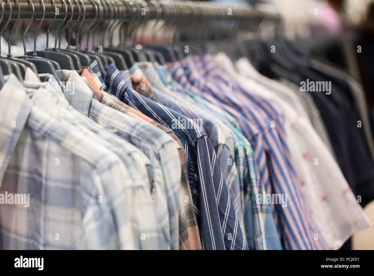 A row of colorful row t-shirts hanging on hangers in t-shirts retail shop. Stock Photo